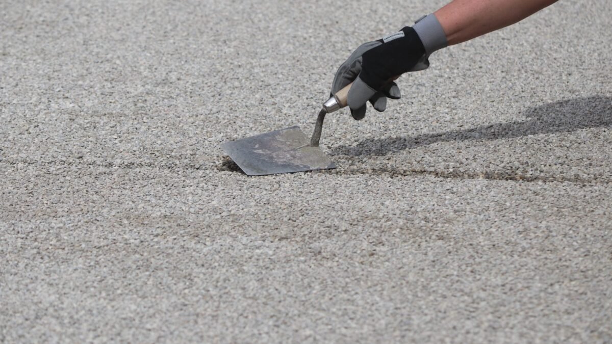 Worker leveling a gravel base with a trowel, part of the cost to pave a driveway