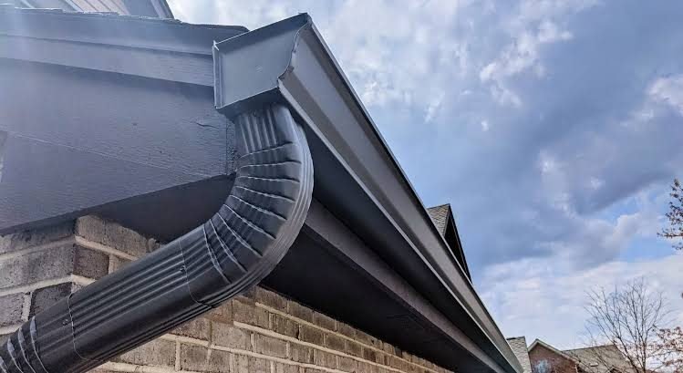 Dark seamless aluminum gutter and downspout on a brick house, from our seamless gutters cost guide