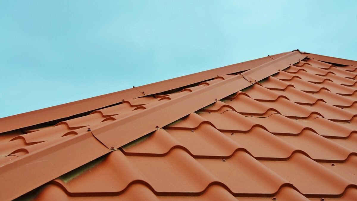 Red steel metal roof panels shaped like tiles against a clear blue sky